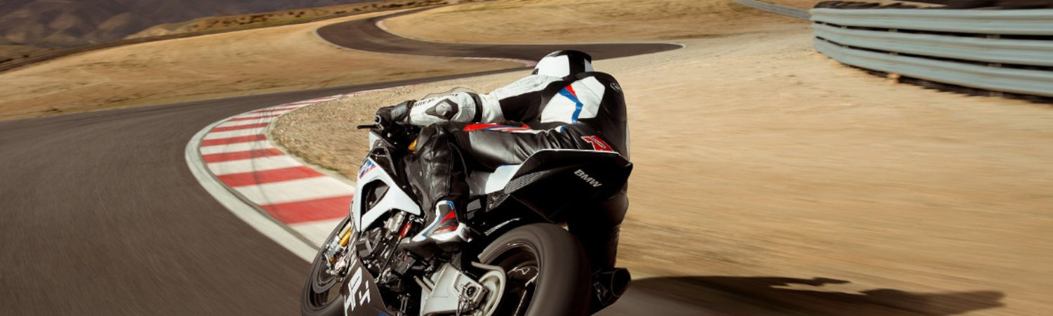 Person with white and black protective gear turning BMW® HP4 RACE bike on a sunny race track. 
